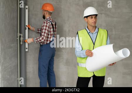 Un architetto con disegni nelle sue mani. L'uomo supervisiona i lavori di costruzione con il costruttore. Caposquadra in casa in costruzione. Un ingegnere di costruzione i Foto Stock