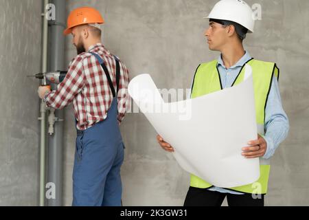 Un architetto con disegni nelle sue mani. L'uomo supervisiona i lavori di costruzione con il costruttore. Caposquadra in casa in costruzione. Un ingegnere di costruzione i Foto Stock