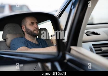 Serios uomo conducente in auto vista laterale specchio, assicurarsi che la corsia è libera prima di fare una svolta. L'espressione del volto umano emozioni. Guida sicura Foto Stock