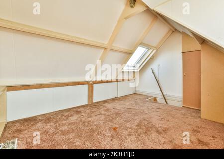 Una camera vuota accogliente e spaziosa in stile mansarda con una piccola finestra Foto Stock