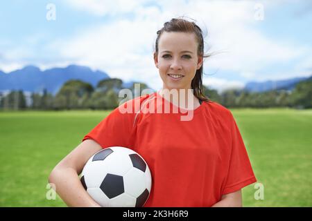 In esso per vincere. Una giovane giocatore di calcio femminile che tiene una sfera di calcio. Foto Stock