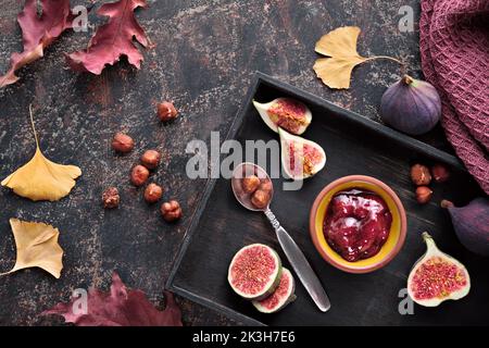 Sfondo ora automatica. Fichi freschi tagliati a metà su vassoio di legno nero. Asciugamano magenta e foglie rosse asciutte d'autunno su tavola testurizzata marrone scuro. Foto Stock