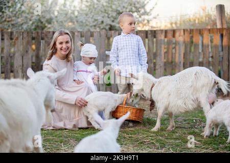 Mamma con una bambina nutre una capra. Donna con bambini in fattoria. Famiglia con capre. Vita di villaggio. Foto Stock