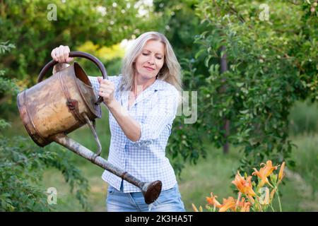 Una donna acqua fiori in giardino, si prende cura del giardino. Foto Stock