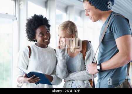 Controllare insieme le date degli esami. Studenti universitari in piedi in un corridoio guardando un libro di testo. Foto Stock