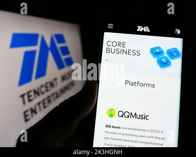 Persona che tiene il cellulare con la pagina web della società Tencent Music Entertainment Group sullo schermo di fronte al logo. Messa a fuoco al centro del display del telefono. Foto Stock