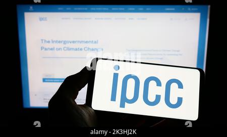 Persona che tiene in mano uno smartphone con il logo del Gruppo intergovernativo sul cambiamento climatico (IPCC) sullo schermo di fronte al sito Web. Messa a fuoco sul display del telefono. Foto Stock