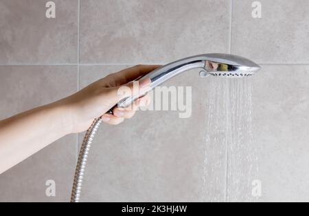 Una donna tiene in mano un soffione doccia contro lo sfondo di una parete del bagno. Spazio di copia per testo, lavaggio Foto Stock