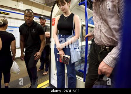 Londra, Inghilterra, Regno Unito. Giovane donna che tiene un libro su un treno della metropolitana Foto Stock