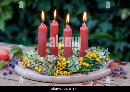 sistemazione con candele e corona di frutti di bosco, fiori di ortensia e rami di bosso Foto Stock