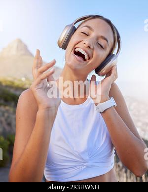 Fitness, cuffie e donna all'aperto ascoltando musica per podcast benessere durante l'allenamento o facendo esercizio sul cielo blu e sul flare delle lenti Foto Stock