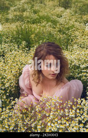 Giovane donna bionda che indossa un abito rosa puffy in un campo di fiori in estate Foto Stock