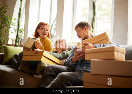 Giovane famiglia felice, genitori e capretto ha ricevuto un ordine in linea, fa gli acquisti di unpacking nel paese. Black Friday o cyber Monday, comfort, tecnologia Foto Stock