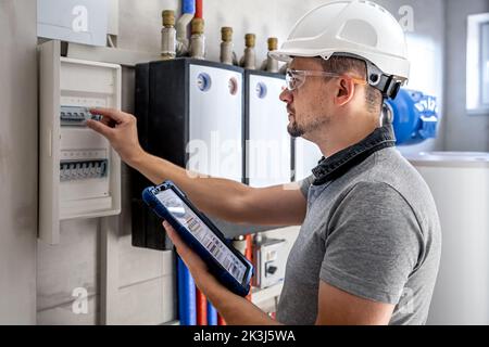 Tecnico elettrico che guarda concentrato mentre lavora in un quadro elettrico con fusibili. Foto Stock