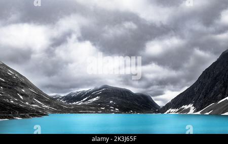 Un lago turchese di acqua dolce sulle montagne norvegesi con un cielo nuvoloso e un po' di neve, orizzontale Foto Stock