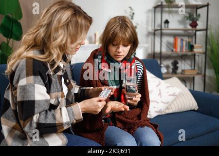 Madre che dà la pillola a sua figlia con influenza. Donna che si prende cura di una ragazza malata Foto Stock