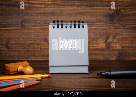 calendario 2023. Sfondo di legno marrone scuro e forniture per ufficio. Foto Stock