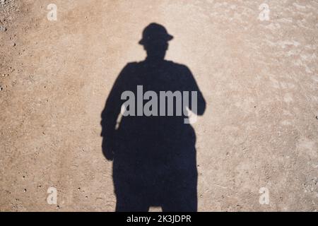 Un'ombra di un uomo a terra in un cappello di ingegneria Foto Stock
