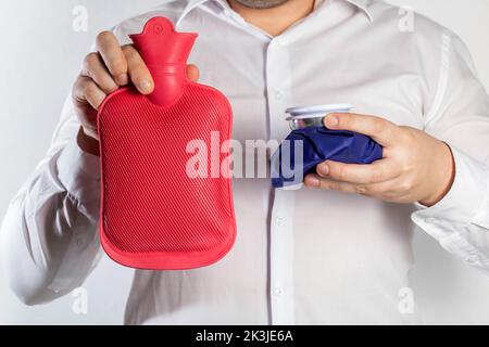 Un uomo in una camicia bianca tiene una borsa di ghiaccio e un pad medico rosso di riscaldamento per l'acqua calda. Il concetto di trattamento termico e freddo Foto Stock