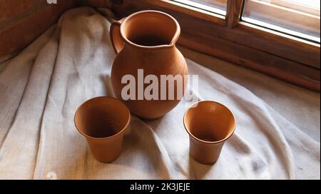 Sul davanzale della finestra si trova l'antica ceramica. Caraffa e tazze di terracotta marrone. Ceramica, primo piano Foto Stock