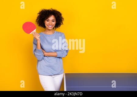 Foto di carino adorabile ragazza riccia vestita blu pullover pronto a giocare a tennis tavolo isolato sfondo di colore giallo Foto Stock