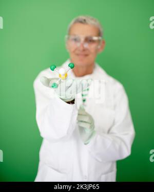scienziato femminile con mantello bianco tiene in mano il modello di molecola e si trova di fronte allo sfondo verde Foto Stock
