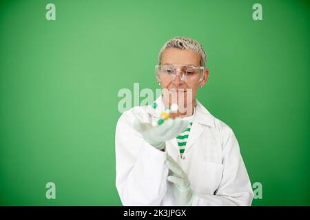 scienziato femminile con mantello bianco tiene in mano il modello di molecola e si trova di fronte allo sfondo verde Foto Stock
