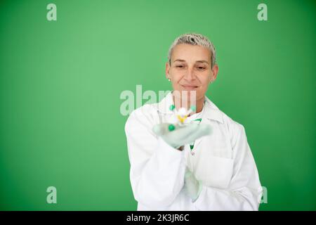scienziato femminile con mantello bianco tiene in mano il modello di molecola e si trova di fronte allo sfondo verde Foto Stock