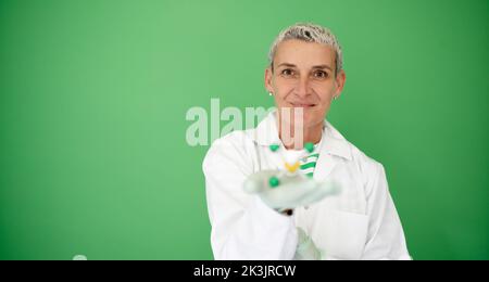 scienziato femminile con mantello bianco tiene in mano il modello di molecola e si trova di fronte allo sfondo verde Foto Stock