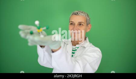 scienziato femminile con mantello bianco tiene in mano il modello di molecola e si trova di fronte allo sfondo verde Foto Stock