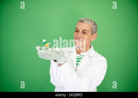 scienziato femminile con mantello bianco tiene in mano il modello di molecola e si trova di fronte allo sfondo verde Foto Stock