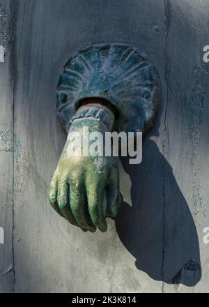 Vista in primo piano della bella annata blu verde battente porta in ottone a forma di mano tenendo la palla isolato sulla porta di legno grigio, Montpellier, Francia Foto Stock