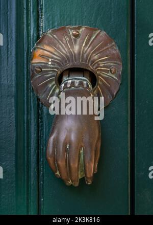 Vista closeup di ottone vintage porta bussare a forma di mano tenendo la palla isolato su antica porta di legno verde scuro, Montpellier, Francia Foto Stock