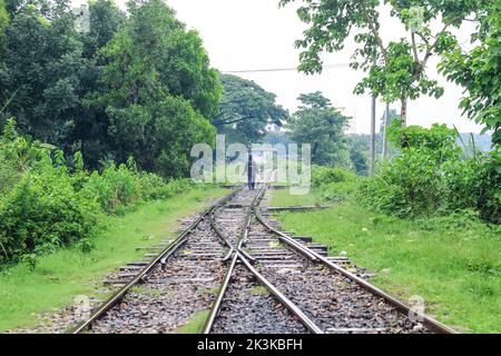 Uomo che cammina sulla ferrovia in una giornata piovosa. Ha un ombrello in mano. Uomo con un ombrello sulla ferrovia, in attesa di nuove avventure e viaggi. Foto Stock