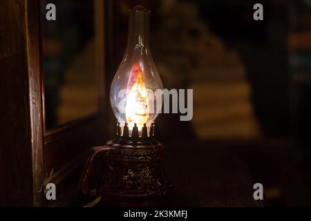 Una lampada di kerosene vintage coperta di polvere e fuliggine, sparata su uno sfondo di pannelli di legno e burlap. Foto Stock