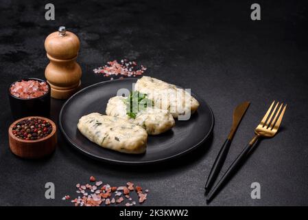 Piatto tradizionale lituano zeppelin, gnocchi di patate bollite farciti con carne macinata, su un piatto di ceramica nera su fondo di cemento scuro Foto Stock