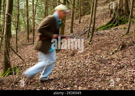 Un'immagine blurida di un uomo che cammina attraverso i boschi è una pistola Foto Stock