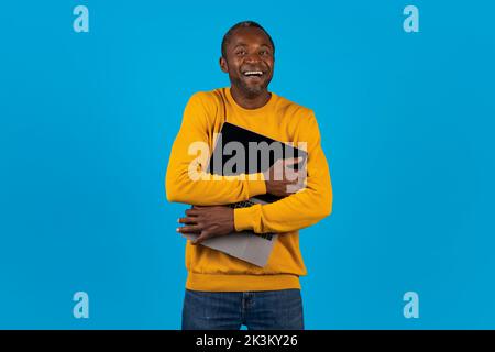 Ridendo uomo afroamericano che abbraccia un computer portatile aperto Foto Stock