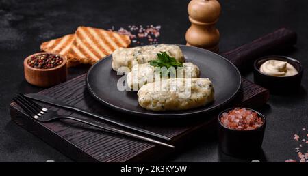 Piatto tradizionale lituano zeppelin, gnocchi di patate bollite farciti con carne macinata, su un piatto di ceramica nera su fondo di cemento scuro Foto Stock