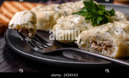 Piatto tradizionale lituano zeppelin, gnocchi di patate bollite farciti con carne macinata, su un piatto di ceramica nera su fondo di cemento scuro Foto Stock