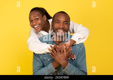 Allegra coppia afroamericana che abbraccia la posa su sfondo giallo Foto Stock