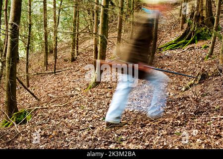 Un'immagine blurida di un uomo che cammina attraverso i boschi è una pistola Foto Stock