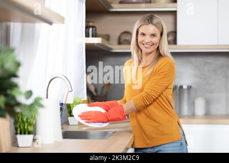 Allegro bella donna bionda lavare piatti a casa Foto Stock