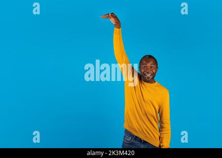 Felice uomo afroamericano che mostra l'altezza di qualcosa di invisibile Foto Stock