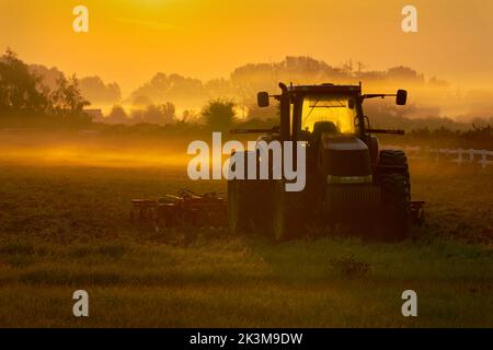 Foggy mattina Farm Field Alba. Colori dell'alba su un campo e trattore di fattoria misty. Foto Stock