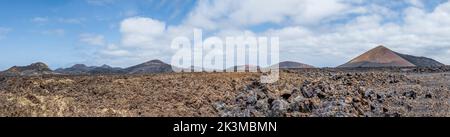 Vista mozzafiato della strada asfaltata che va vicino alle vette di montagna contro il cielo nuvoloso blu nelle giornate di sole a Caldera de Los Cuervos a Lanzarote, Spagna Foto Stock