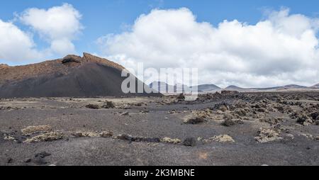 Vista mozzafiato della strada asfaltata che va vicino alle vette di montagna contro il cielo nuvoloso blu nelle giornate di sole a Caldera de Los Cuervos a Lanzarote, Spagna Foto Stock