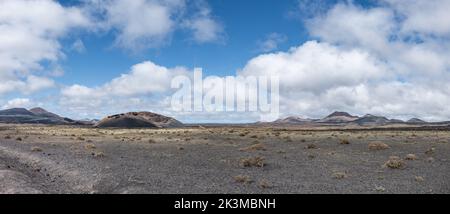 Vista mozzafiato della strada asfaltata che va vicino alle vette di montagna contro il cielo nuvoloso blu nelle giornate di sole a Caldera de Los Cuervos a Lanzarote, Spagna Foto Stock