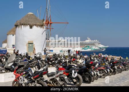 Mykonos, Grecia - 2022 maggio: File di moto parcheggiate vicino ai famosi mulini a vento tradizionali in una fila sull'isola greca di Mykonos. Foto Stock