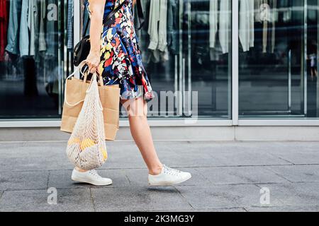 Sostenibile Eco friendly Slow Fashion Shopping. Ritratto di donna senza volto con borsa in rete bianca riutilizzabile in tela e borsa della spesa in carta nel negozio di abbigliamento Foto Stock